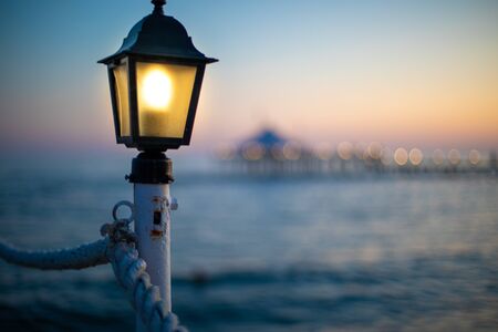 a lantern on a bathing jetty glows bright yellow at duskの写真素材