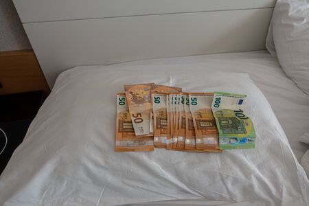 many euro banknotes are spread out on a bed with a white duvet coverの写真素材