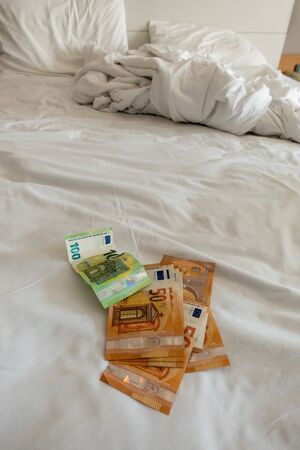 many euro banknotes are spread out on a bed with a white duvet coverの写真素材