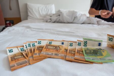 many euro banknotes are spread out on a bed with a white duvet coverの写真素材
