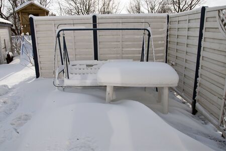 a thick white blanket of snow covers garden furniture standing on a terraceの写真素材