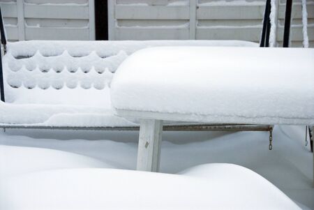 a thick white blanket of snow covers garden furniture standing on a terraceの写真素材