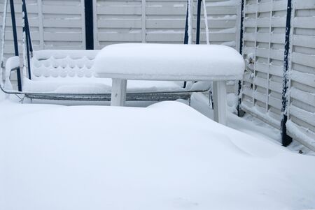 a thick white blanket of snow covers garden furniture standing on a terraceの写真素材
