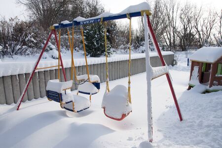 a thick white blanket of snow covers a children's swingの写真素材