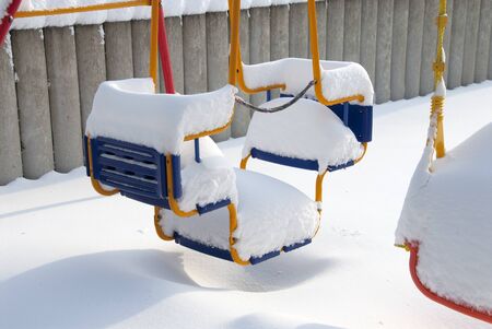 a thick white blanket of snow covers a children's swingの写真素材