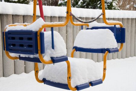 a thick white blanket of snow covers a children's swingの写真素材