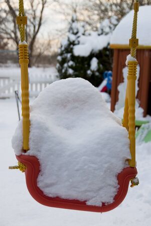 a thick white blanket of snow covers a children's swingの写真素材