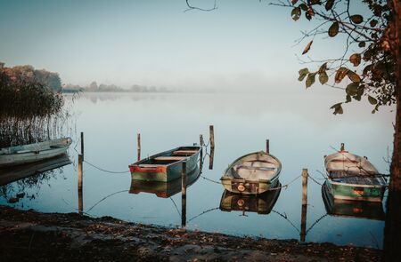 on a lake some rowboats are moored and on the lake there is fog and the lake is quite calmの写真素材