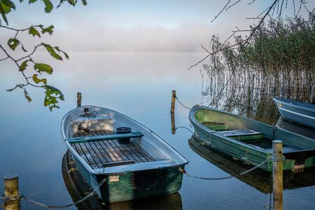 on a lake some rowboats are moored and on the lake there is fog and the lake is quite calmの写真素材