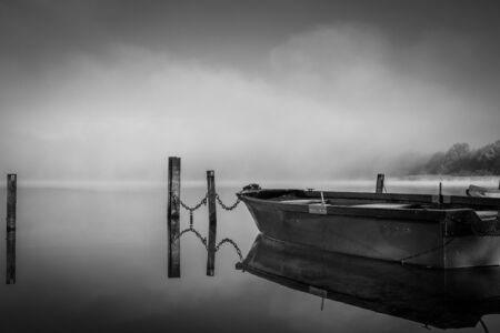 on a lake some rowboats are moored and on the lake there is fog and the lake is quite calmの写真素材