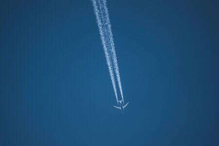 a large passenger aircraft flies in the cloudless blue sky and produces a white glowing condensation trailの写真素材
