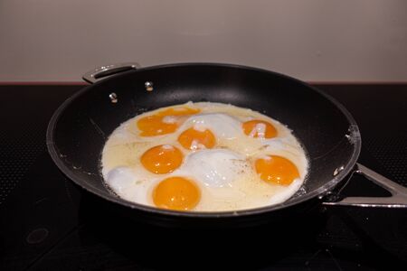 fry in a black round frying pan 6 fried eggsの写真素材
