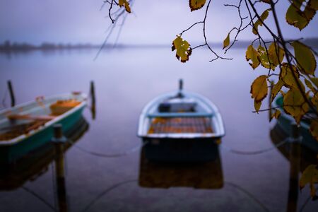 on a lake there are several rowing boats on the shore and they are chained and the water is mirror-smoothの写真素材