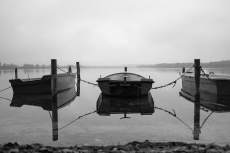 on a lake there are several rowing boats on the shore and they are chained and the water is mirror-smoothの写真素材