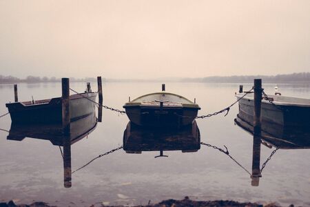 on a lake there are several rowing boats on the shore and they are chained and the water is mirror-smoothの写真素材