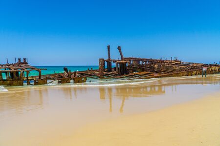 on the beach of fraser island lies the skeleton of a washed-up shipwreck in fine weatherの写真素材