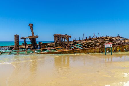 on the beach of fraser island lies the skeleton of a washed-up shipwreck in fine weatherの写真素材
