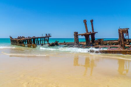 on the beach of fraser island lies the skeleton of a washed-up shipwreck in fine weatherの写真素材