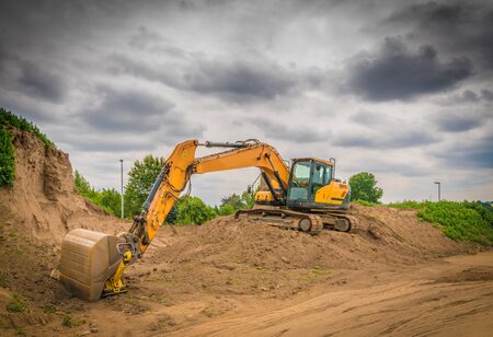  a yellow excavator stands on a mound of earth on a large construction site