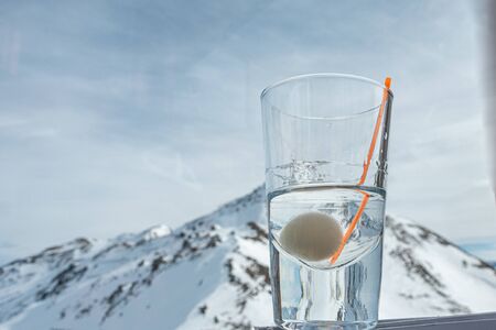 on a table stands a glass with alcohol and in the background are the snow-covered mountains