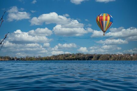 a colourful hot air balloon flies over the blue water of a lakeの写真素材