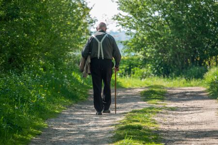 an old man walks along a country lane on a walking stickの写真素材