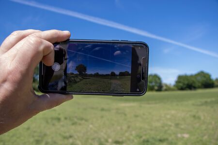 one hand holds a smartphone in his hand and photographs a landscape