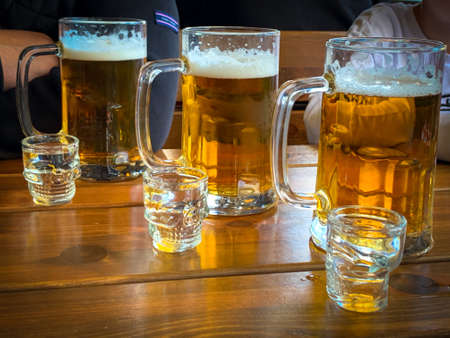 on a table are three big glasses of beer and next to it are 3 glasses of vodkaの写真素材