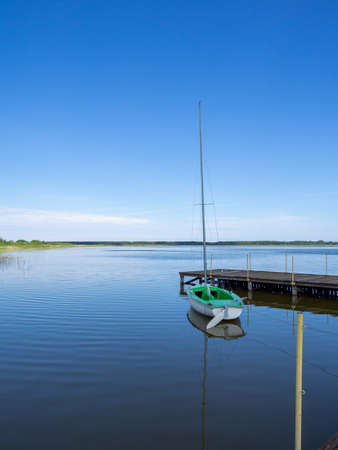 A small green sailing boat is attached to a lake at a landing stage
