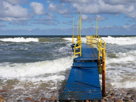 a blue wooden footbridge with yellow railings leads into the Baltic Seaの写真素材