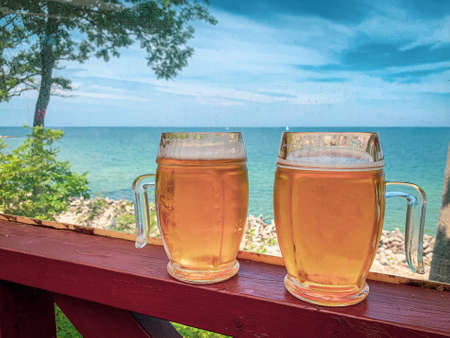 two beer glasses stand side by side and behind them is the sea