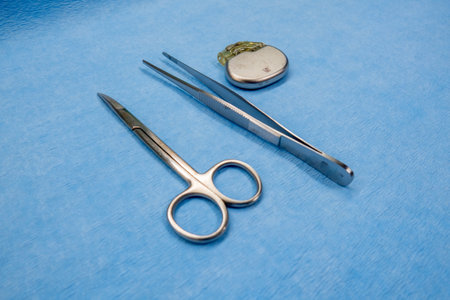 a pacemaker, scissors and tweezers on a blue surgical pad
