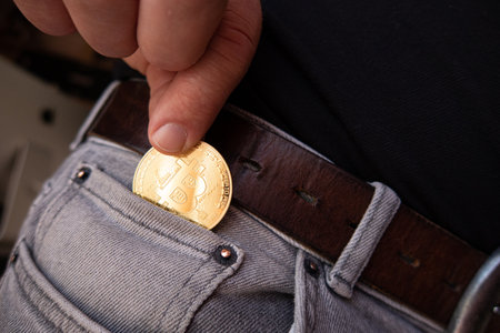a golden Bitcoin coin is put into a gray trouser pocketの写真素材