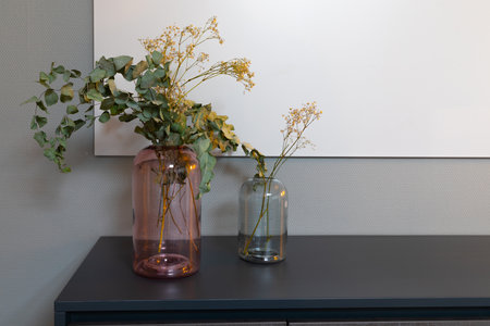 put dry plants in two glass vases standing next to each otherの写真素材