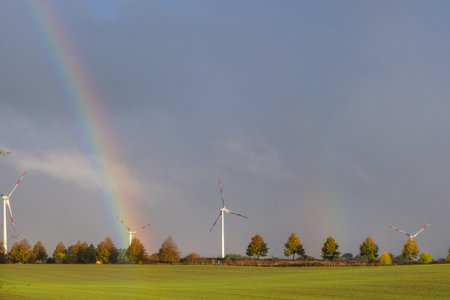 a big rainbow over a field on which wind turbines standの写真素材