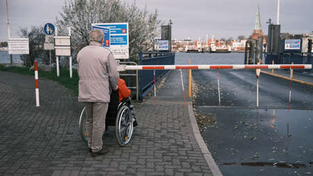 an old man is standing at a harbor with his wife, who is in a wheelchair