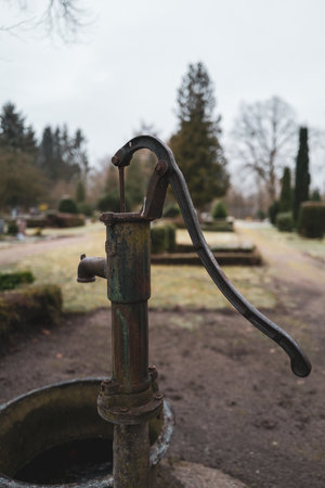 next to an old water pump stands a stand with different watering cans on a cemeteryの写真素材