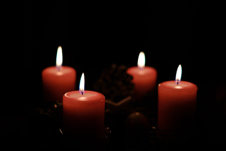 a close up of a burning red candle and the background is dark