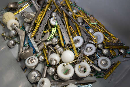 many explanted titanium plates, screws and hip prostheses lie in a gray plastic boxの写真素材