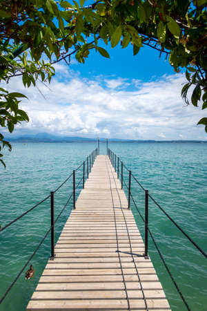 a wooden footbridge leads onto the turquoise Garda Lakeの写真素材