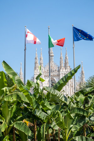 in front of the Milan Cathedral the Italian, English and European flags are flyingの写真素材