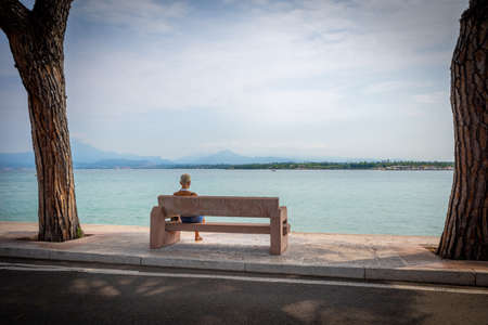 a woman sitting on a bench at lake gardaの写真素材