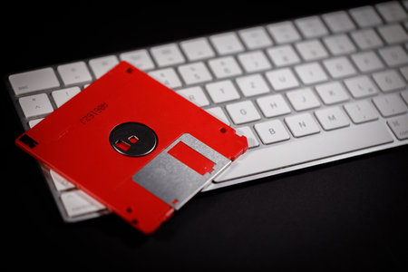 a red floppy disk lies on a white keyboardの写真素材