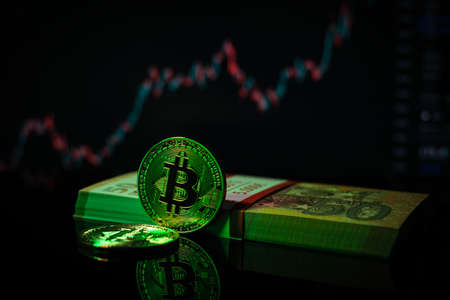 a bitcoin coin lies next to the pile of banknotes and in the background is a rising bitcoin chart