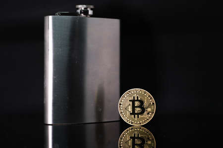 a bitcoin coin stands next to a steel hip flask