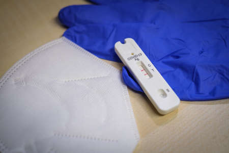one positive corona rapid test lies next to a medical face mask and a blue medical glove