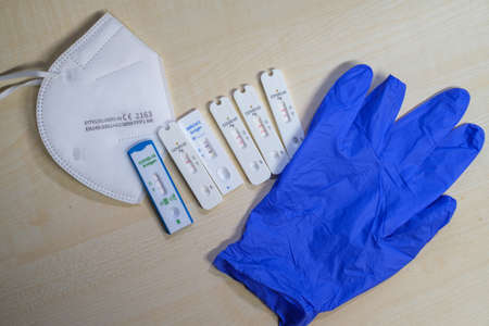 6 positive corona rapid tests lie next to a medical face mask and a blue medical glove
