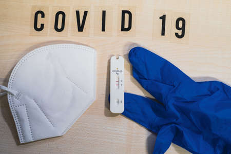 one positive corona rapid test lies next to a medical face mask and a blue medical glove