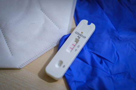 one positive corona rapid test lies next to a medical face mask and a blue medical glove