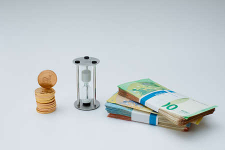 a stack of gold coins stands next to an hourglass and a stack of euro banknotesの写真素材